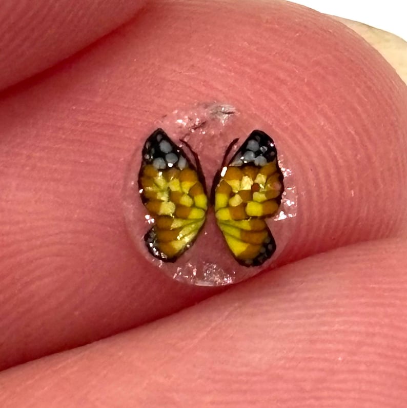 Tiny orange and black butterfly murrini resting on a fingertip